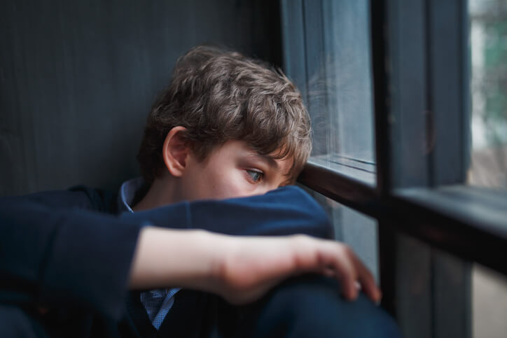 A sad teenage boy sitting by the window